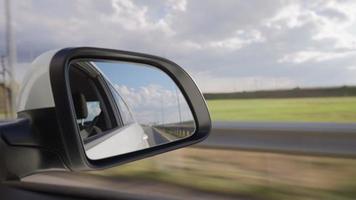 Blick vom Seitenspiegel auf das Innere eines fahrenden Autos entlang der Autobahn an einem sonnigen Tag. Konzept von Fahrzeugen und Transport. keine Leute. video