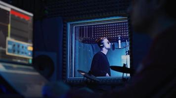 el cantante de rap masculino con auriculares y el ingeniero de sonido están creando una nueva canción en un estudio de grabación profesional. programa y herramientas para crear música en el monitor de la computadora. trabajar en la sala de grabación de música video