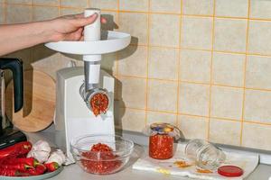 cocinar adjika de pimiento picante y ajo molido en una picadora de carne. preparativos para el invierno. remedio popular para la gripe y los resfriados foto