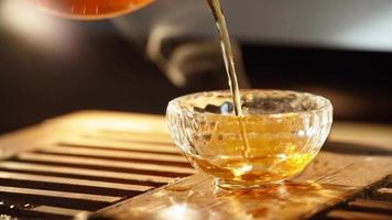 Herbal Chinese Tea Poured into Beautiful Transparent Glass against background of the smoke coming from scented sticks, backlit by warm light. Tea ceremony. Oriental cup close up. Unrecognizable person video