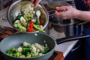 mujer caucásica mayor vierte verduras en una sartén del colador de acero inoxidable foto