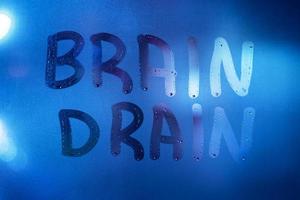 the words brain drain written on night wet window glass close-up with blurred background in classic blue color photo