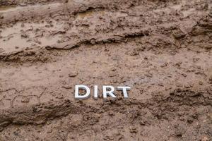 la palabra suciedad puesta con letras plateadas en la superficie húmeda de la carretera de tierra - primer plano con enfoque selectivo foto