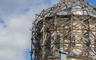 gray wood scaffolds on architectural dome at day light on blue sky with white clouds photo