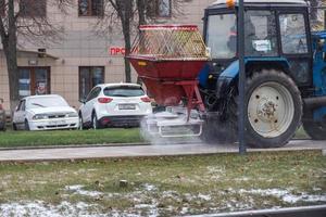 tula, rusia - 21 de noviembre de 2020, tractor esparciendo reactivo de sal en el pavimento de la ciudad a la luz del día de invierno. foto