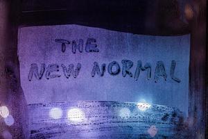 words the new normal handwritten on foggy night window glass surface photo