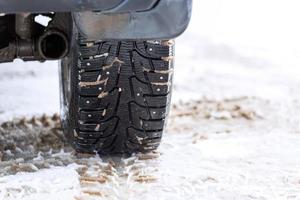 an unadorned picture of winter car wheel with metal spikes on snow close-up photo