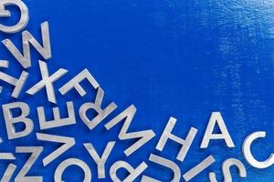 fondo plano abstracto de caracteres alfabéticos de metal plateado sobre fondo azul con la mitad del relleno del marco y espacio de copia foto