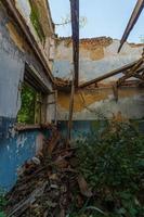 ventana de madera rota y habitación con hierba alta, vista dentro de un dormitorio abandonado medio destruido a la luz del día de verano foto