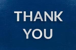 the words thank you laid with aluminium white metal letters on painted flat blue background - directly above in flat lay composition photo