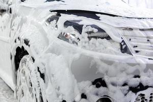 a car covered by soap foam while washing indoors - close-up front wiew with selective focus photo