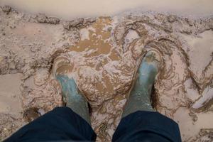 feet in green rubber boots stands in wet brown mud directly above view photo