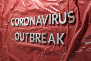 las palabras brote de coronavirus se colocaron con letras de metal plateado en una película de plástico roja arrugada foto