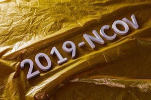 la palabra 2019-ncov colocada con letras de metal sobre fondo de película plástica arrugada amarilla en composición diagonal inclinada foto