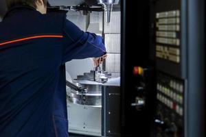 The operator of 5-axis cnc milling machine changes the workpiece in a collet chuck. Selective focus on background. photo