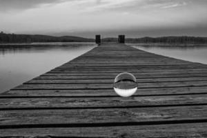 Glass ball on a wooden pier at a Swedish lake at dusk in black and white. Nature photo