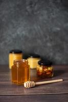 varios tarros de miel sobre un fondo oscuro. miel con nueces. un palito de miel. con espacio para texto. foto
