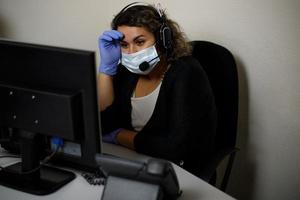 A call center agent working on the support hotline in the office, wearing a mask and gloves. The call center operator is talking to the customer. photo