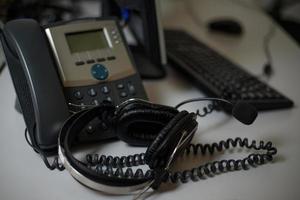 Stationary phone and headset on desk indoors, closeup. Communication support, call center and customer support service. photo