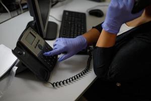 un empleado de la oficina hace una llamada en un teléfono fijo con guantes. primer plano del teléfono. en tonos grises. protección, virus.teléfono estacionario y auriculares en el escritorio en el interior, primer plano. foto