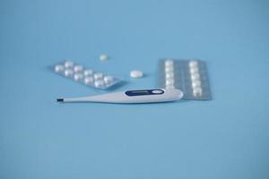 Top view of medicines, thermometer on a blue, blue background. He was lying flat. First aid kit - pills, thermometer, drops. Flat lying. Tablets in a package. Tablets are white and yellow. photo
