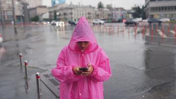 Woman in pink hooded poncho navigates a city street in the rain video