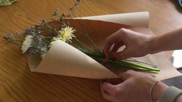 florista embrulha buquê de flores em papel pardo e barbante video