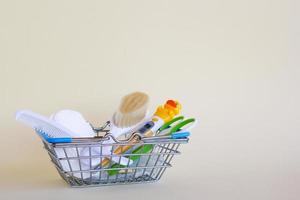 Shopping basket with baby care items - scissors, two hairbrushes, thermometer, cotton pads and nasal aspirator - on a beige background with copy space. Concept of medicine and hygiene of the child. photo