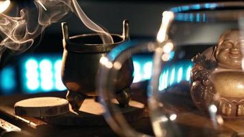 Black Hot Tea Poured into Beautiful Glass against background of the Smoke Coming from Scented Sticks, backlit by Warm Light. Tea ceremony. Oriental Cup close up. Unrecognizable person. Slow motion video