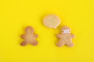 Galletas caseras de pan dulce con glaseado blanco sobre fondo amarillo, vista superior. dos hombres, uno de ellos con mascarilla y con nube de llamadas. foto