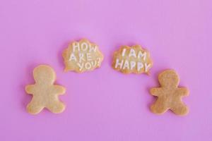 galletas de mantequilla caseras con glaseado blanco sobre fondo rosa, vista superior. dos personas con una nube de llamadas con texto - cómo estás - y - estoy feliz foto