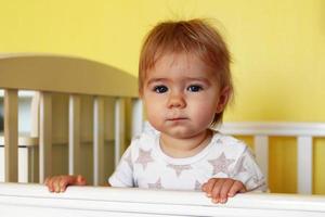 linda niña de un año con ojos azules y cabello rubio acaba de despertarse por la mañana en su cama. foto