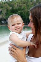 retrato de una hermosa joven madre europea abrazando a su pequeña hija en un fondo de playa tropical. foto