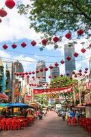 kuala lumpur, malasia, 22 de febrero de 2020. vista en una calle concurrida con cafés, tiendas locales y farolillos rojos chinos en un fondo del centro con rascacielos. foto