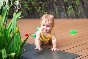 Little girl tries to crawl on a floor in playground with green plants and colorful toys. photo