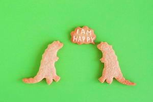 galletas de mantequilla caseras en forma de dinosaurios con una nube de llamadas con texto - estoy feliz - sobre fondo verde, vista superior. foto