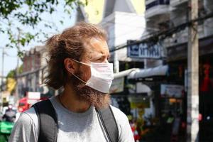 Handsome young European man is walking in the city with medical face mask for protect himself from coronavirus disease, influenza virus or smog. photo