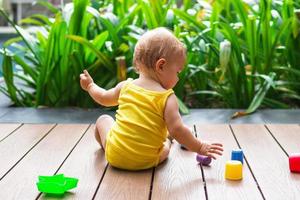 niña sonriente jugando al aire libre con un colorido constructor de plástico sobre un fondo de plantas verdes y piscina. vista trasera. foto