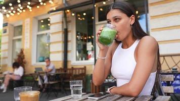 Frau nippt an grünem Matcha-Tee-Latte am Café-Tisch im Freien video