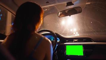 mulher está dirigindo um carro à noite ao longo de uma estrada iluminada por lanternas. há uma tela verde no painel de trabalho do carro. conceito de transporte e veículo. viajando na estrada. video