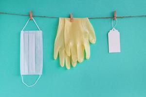 Drying of medical face mask and disposable gloves after washing on a rope for reuse, on a turquoise background with empty blank paper tag for text. Concept of new normal lifestyle. photo