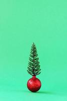 Shiny red ball with artificial Christmas tree on green background with copy space. Minimal Christmas and New Year concept. photo