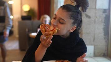 Young woman eats a slice of pizza inside a restaurant video