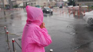 mujer en poncho rosa con capucha navega por una calle de la ciudad bajo la lluvia video