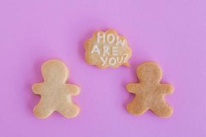 galletas de mantequilla caseras con glaseado blanco sobre fondo rosa, vista superior. dos personas con una nube de llamadas con texto - ¿cómo estás? foto