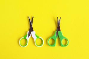 Two open baby green scissors on yellow background, flat lay with copy space. Baby care concept. photo