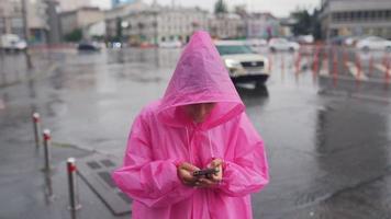 vrouw in roze met een kap poncho navigeert een stad straat in de regen video