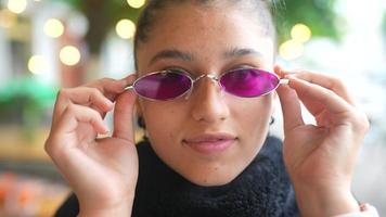 Cerca de una joven poniéndose gafas de sol ovaladas de color púrpura