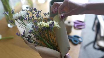 florista embrulha buquê de flores em papel pardo e barbante video