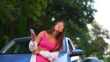 Woman leans on hood of car checking phone looking for help video